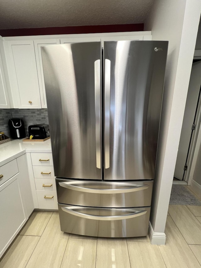 interior details featuring a textured ceiling, white cabinetry, tasteful backsplash, and stainless steel refrigerator