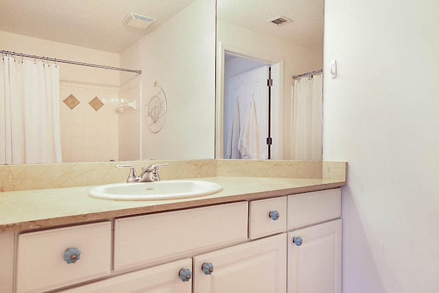 bathroom with a textured ceiling, walk in shower, and vanity