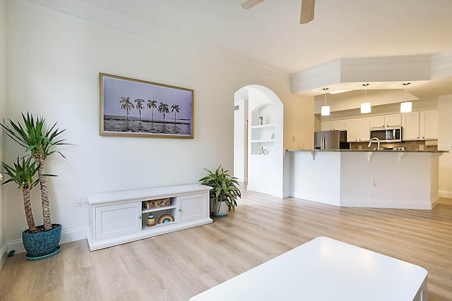 living room featuring ceiling fan, built in shelves, crown molding, and light hardwood / wood-style flooring