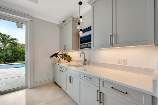 kitchen with sink, light stone counters, light tile patterned flooring, ornamental molding, and hanging light fixtures