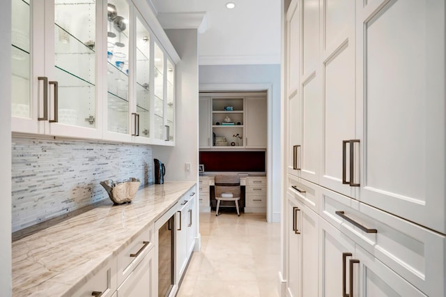 bar featuring white cabinetry, ornamental molding, backsplash, and light stone countertops