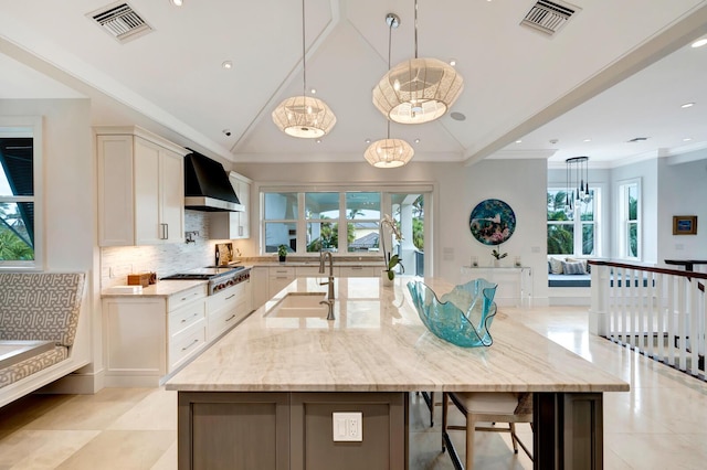 kitchen with wall chimney exhaust hood, decorative light fixtures, a large island, white cabinetry, and sink