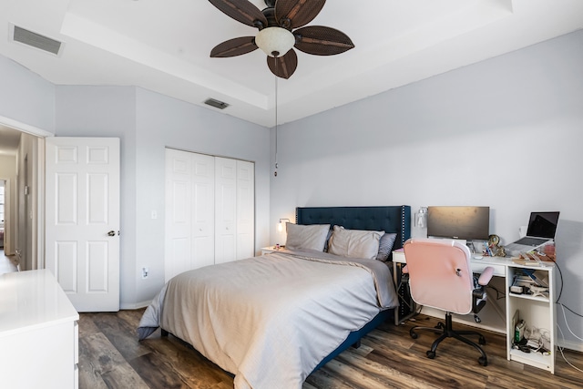 bedroom with dark hardwood / wood-style flooring, a closet, a raised ceiling, and ceiling fan