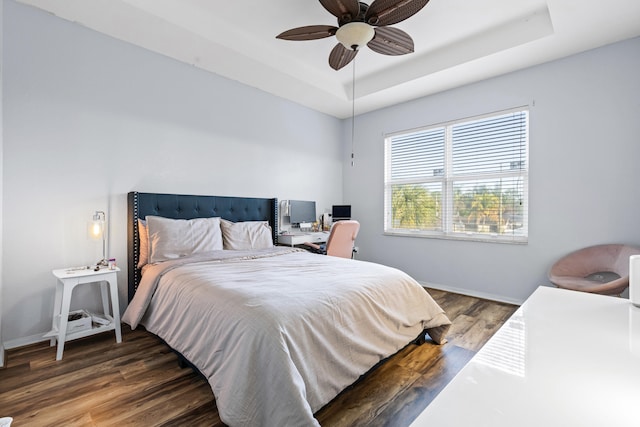 bedroom featuring dark hardwood / wood-style floors, ceiling fan, and a tray ceiling