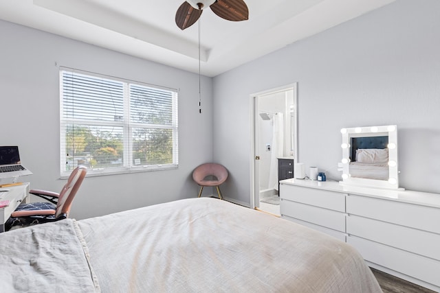 bedroom featuring ceiling fan, ensuite bath, and a tray ceiling