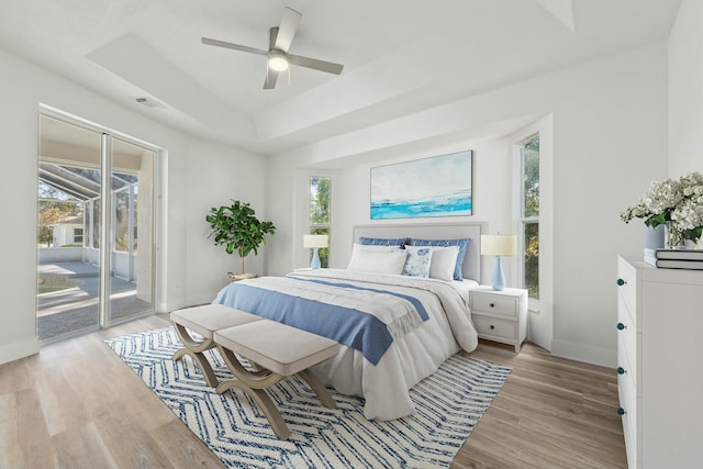 bedroom featuring ceiling fan, light hardwood / wood-style floors, a raised ceiling, and access to outside