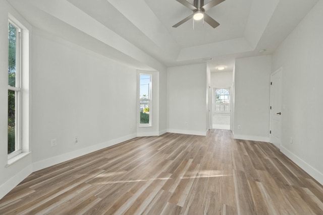 empty room featuring a raised ceiling, ceiling fan, and light hardwood / wood-style flooring