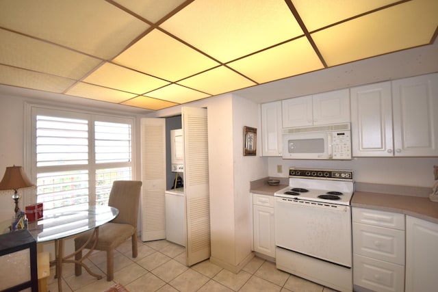 kitchen with light tile patterned flooring, white appliances, white cabinetry, and stacked washer and clothes dryer