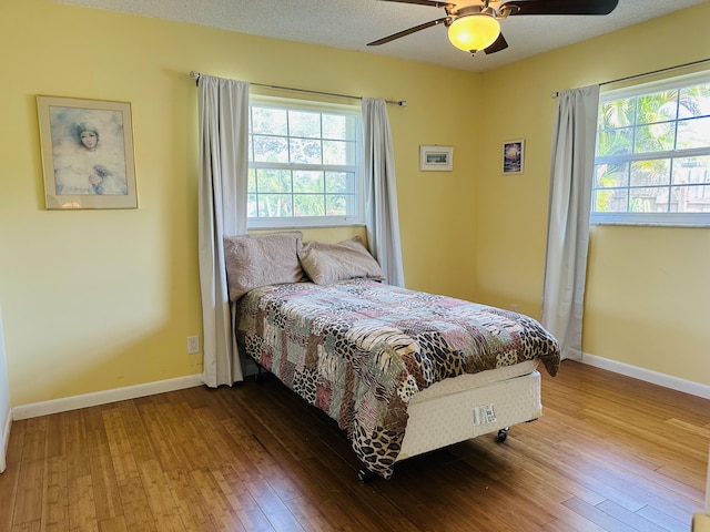 bedroom with ceiling fan, hardwood / wood-style flooring, and multiple windows