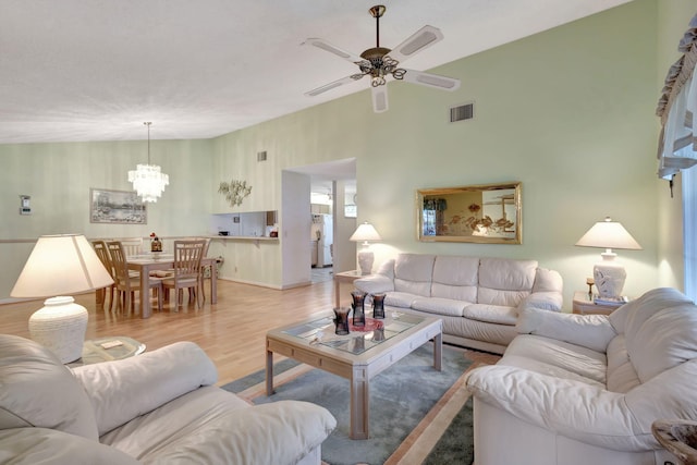 living room with vaulted ceiling, ceiling fan with notable chandelier, and light hardwood / wood-style floors