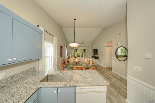 kitchen with dishwasher, sink, blue cabinetry, vaulted ceiling, and light stone counters