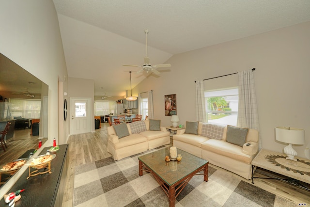 living room with ceiling fan, a wealth of natural light, lofted ceiling, and light wood-type flooring