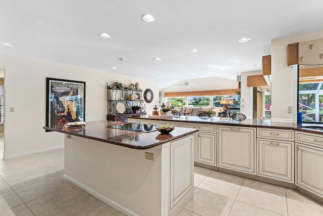 kitchen featuring light tile patterned floors, dark stone countertops, a kitchen island, black electric stovetop, and cream cabinetry