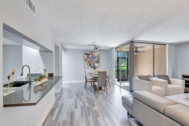 living room featuring light hardwood / wood-style floors, floor to ceiling windows, ceiling fan, a textured ceiling, and sink