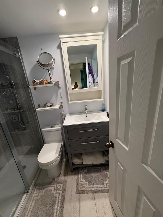 bathroom featuring a shower with door, vanity, wood-type flooring, and toilet