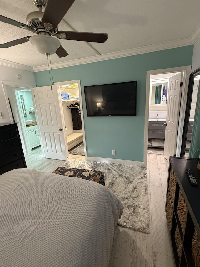 bedroom featuring ensuite bath, a walk in closet, crown molding, light wood-type flooring, and a closet