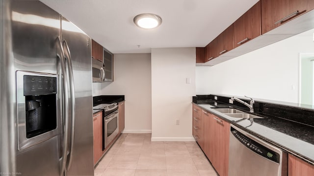 kitchen featuring stainless steel appliances, dark stone countertops, light tile patterned floors, and sink