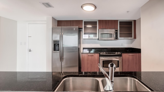 kitchen with appliances with stainless steel finishes, dark stone countertops, and sink