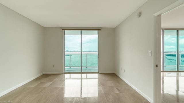 unfurnished room featuring a water view, a wall of windows, and plenty of natural light