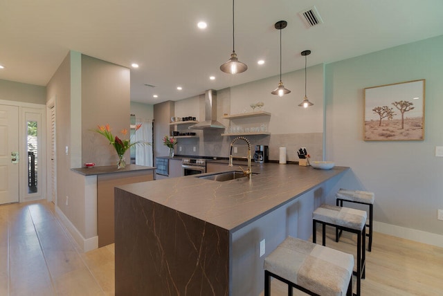 kitchen featuring wall chimney range hood, a breakfast bar, kitchen peninsula, sink, and hanging light fixtures