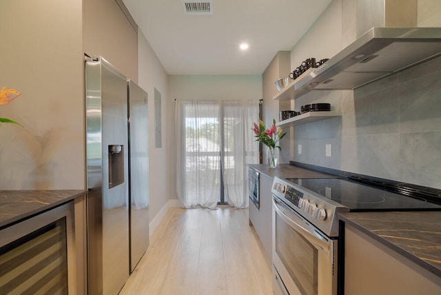 kitchen featuring wine cooler, wall chimney range hood, dark stone countertops, light hardwood / wood-style floors, and stainless steel appliances