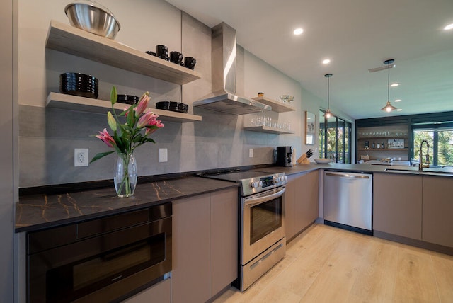 kitchen featuring pendant lighting, wall chimney exhaust hood, stainless steel appliances, sink, and light wood-type flooring