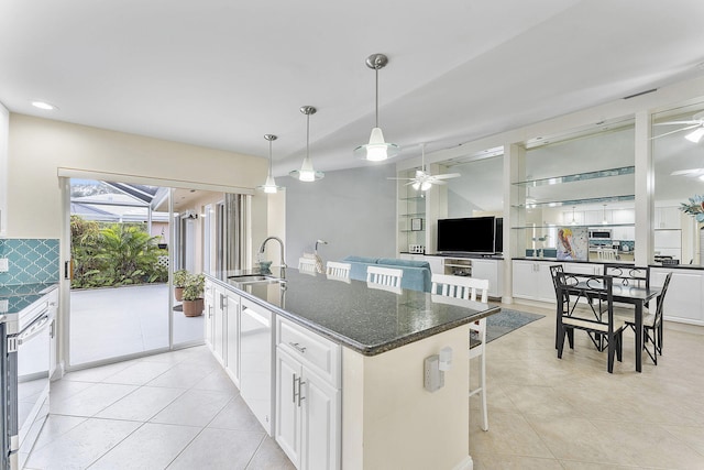 kitchen with a kitchen bar, an island with sink, dark stone counters, white cabinets, and sink