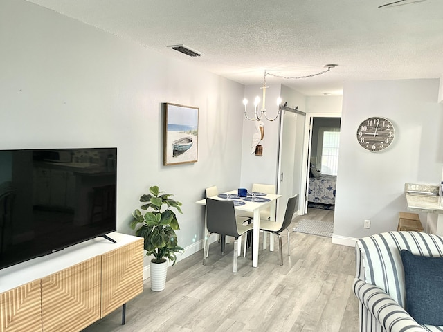 dining space featuring a textured ceiling, a chandelier, a barn door, and light hardwood / wood-style flooring