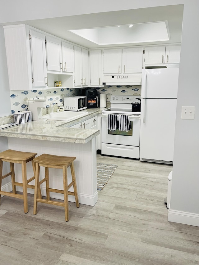 kitchen with backsplash, a breakfast bar, kitchen peninsula, white appliances, and white cabinetry