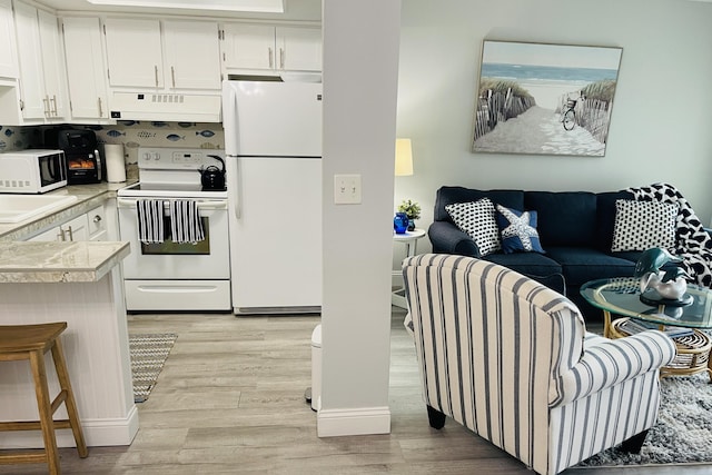 kitchen with white cabinets, sink, white appliances, and light hardwood / wood-style flooring