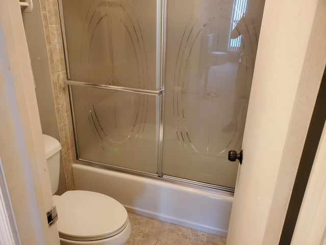 bathroom featuring tile patterned flooring, bath / shower combo with glass door, and toilet