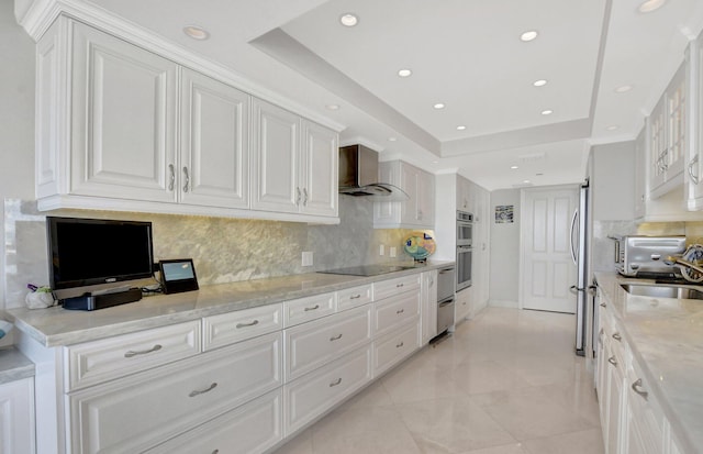 kitchen with light stone counters, white cabinetry, a tray ceiling, and wall chimney exhaust hood