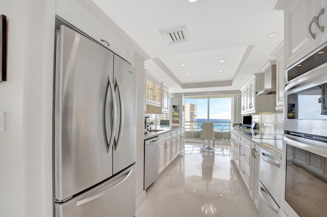 kitchen featuring a tray ceiling, white cabinets, appliances with stainless steel finishes, and a water view