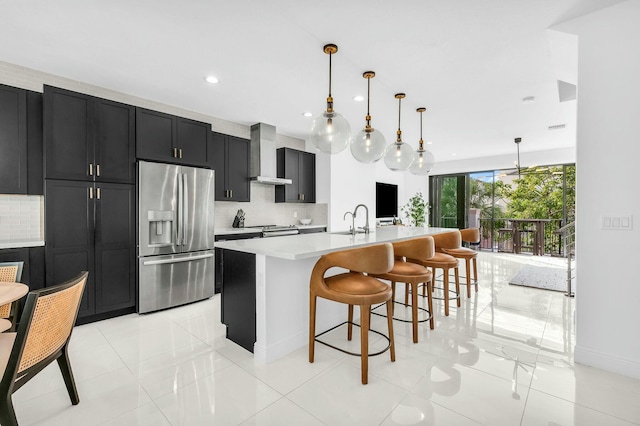 kitchen with appliances with stainless steel finishes, pendant lighting, a kitchen bar, wall chimney range hood, and a center island with sink