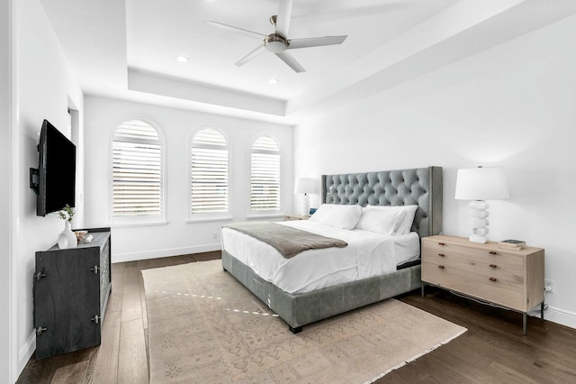 bedroom with ceiling fan, dark wood-type flooring, and a tray ceiling