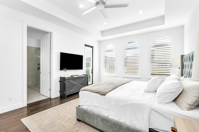 bedroom with ceiling fan, ensuite bathroom, dark hardwood / wood-style flooring, and a tray ceiling