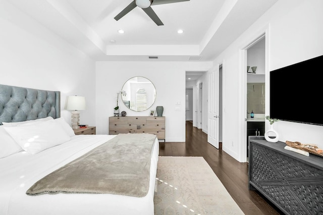 bedroom featuring ceiling fan, a tray ceiling, dark hardwood / wood-style flooring, and ensuite bathroom