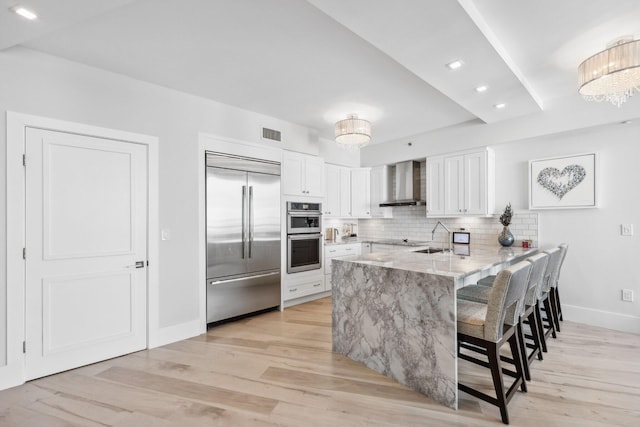 kitchen featuring stainless steel appliances, wall chimney exhaust hood, white cabinets, and kitchen peninsula