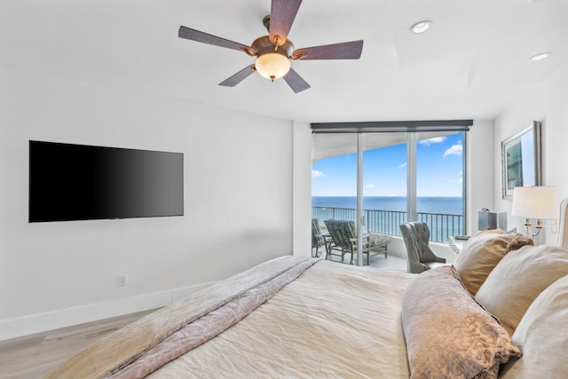 bedroom with ceiling fan, access to outside, light wood-type flooring, a water view, and a wall of windows