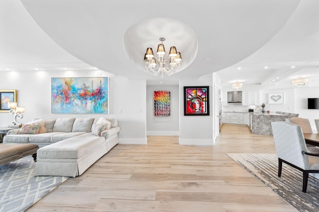 living room featuring an inviting chandelier, light hardwood / wood-style flooring, and a raised ceiling