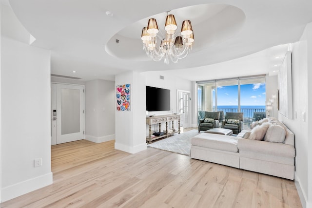 living room with light hardwood / wood-style floors, a wall of windows, a raised ceiling, and an inviting chandelier