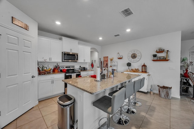 kitchen featuring light stone counters, stainless steel appliances, a center island with sink, a breakfast bar, and white cabinets