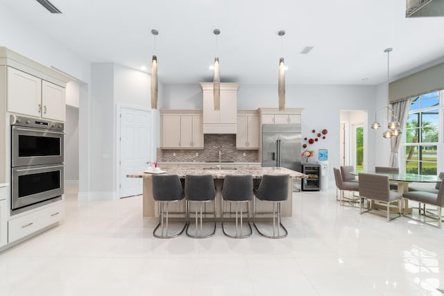 kitchen with appliances with stainless steel finishes, decorative light fixtures, backsplash, an island with sink, and wine cooler