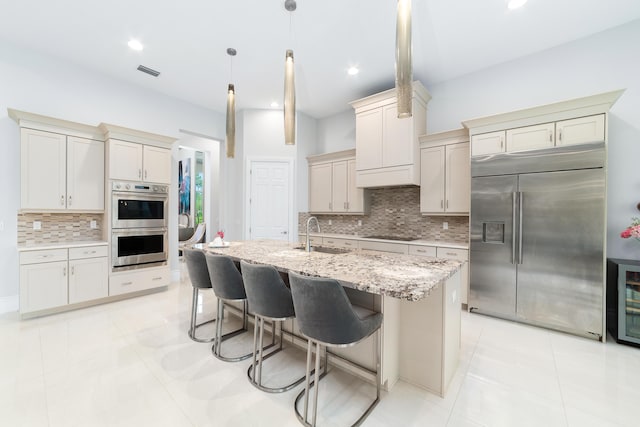 kitchen with sink, decorative light fixtures, an island with sink, stainless steel appliances, and a breakfast bar area