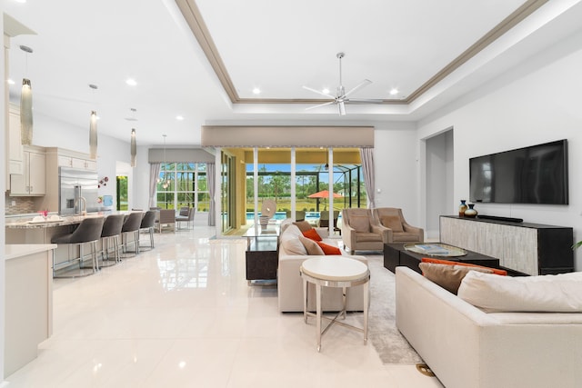 living room with ceiling fan, a raised ceiling, crown molding, and light tile patterned floors