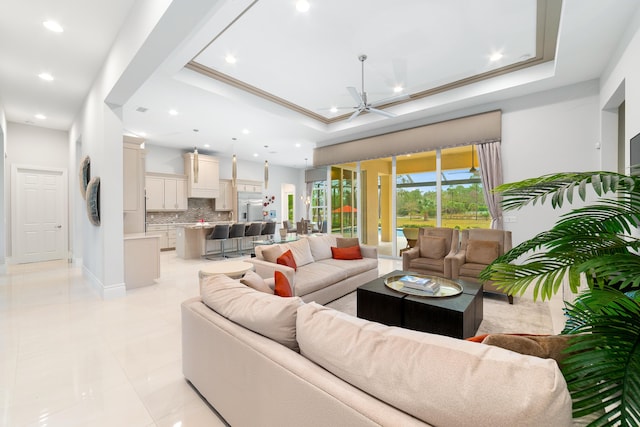 living room featuring ceiling fan, crown molding, light tile patterned floors, and a raised ceiling