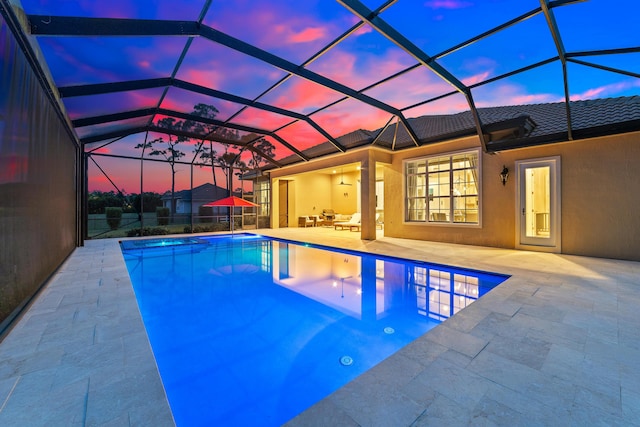 pool at dusk with glass enclosure, a patio, an outdoor living space, and ceiling fan