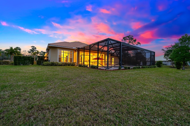 back house at dusk featuring a lawn and a lanai