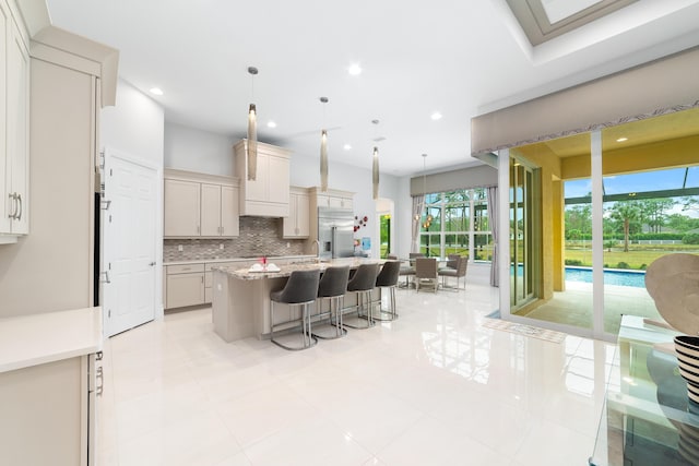 kitchen with a kitchen island with sink, a kitchen breakfast bar, pendant lighting, backsplash, and light stone counters