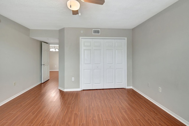 unfurnished bedroom with ceiling fan with notable chandelier, hardwood / wood-style flooring, and a closet